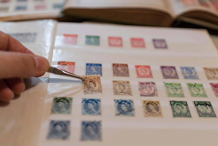 Stamp collection, philately. Man places a postage stamp in an album. Photograph by Malcolm P Chapman