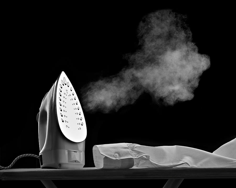 Steaming flat iron and shirt sleeve in front of black background Photograph by Westend61