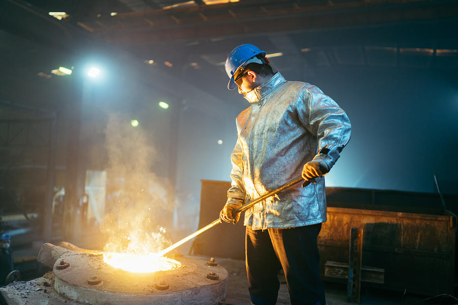 Steel worker in protective clothing raking furnace in an industry Photograph by RainStar