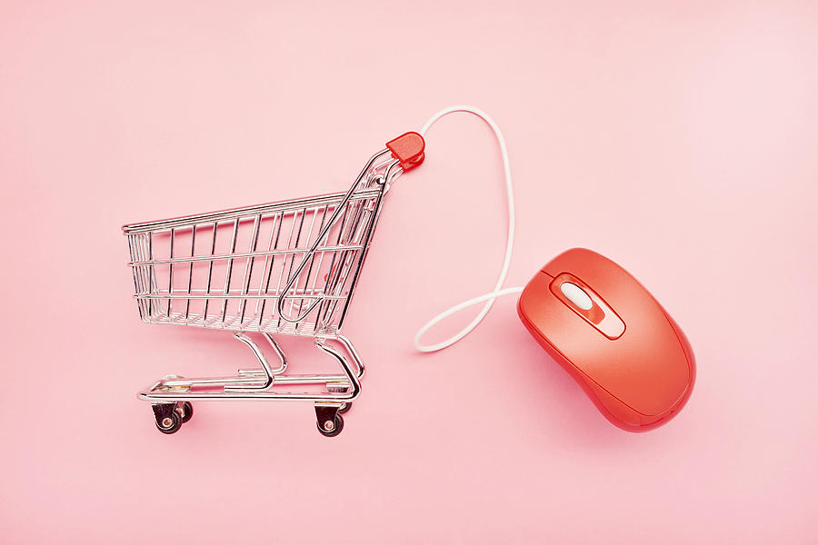 Still life of a small shopping cart and red computer mouse on pink background, online shopping Photograph by The_burtons