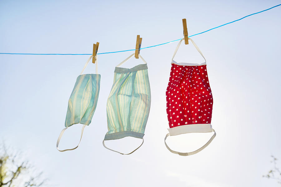 Still life of face masks hanging at clothesline against clear sky and sun, DIY sewing project Photograph by The_burtons