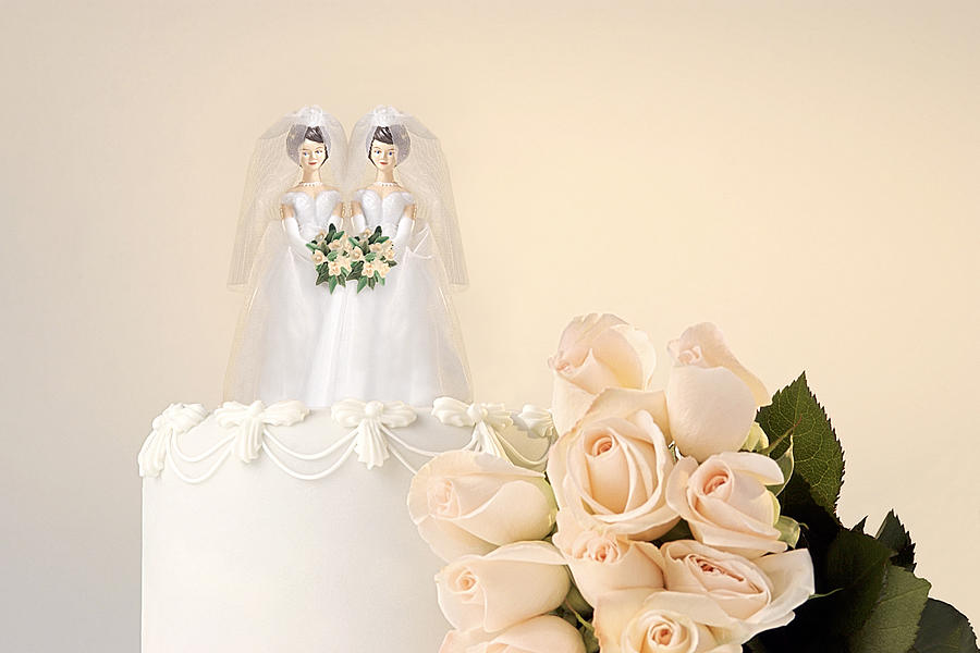 Still life of the top of a wedding cake with two miniature brides cake topper and roses at the side Photograph by Thinkstock