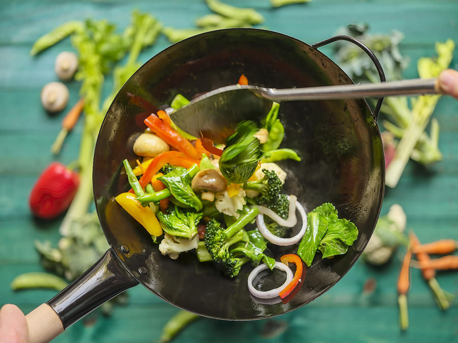 Stir frying and sauteing a variety of fresh colorful market vegetables in a hot steaming wok with vegetables on on a turquoise colored wood table background below the wok. Photograph by Enviromantic