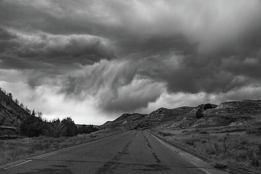 Storm clouds with road at Theodore Roosevelt National Park in North Dakota in black and white Photograph by Eldon McGraw