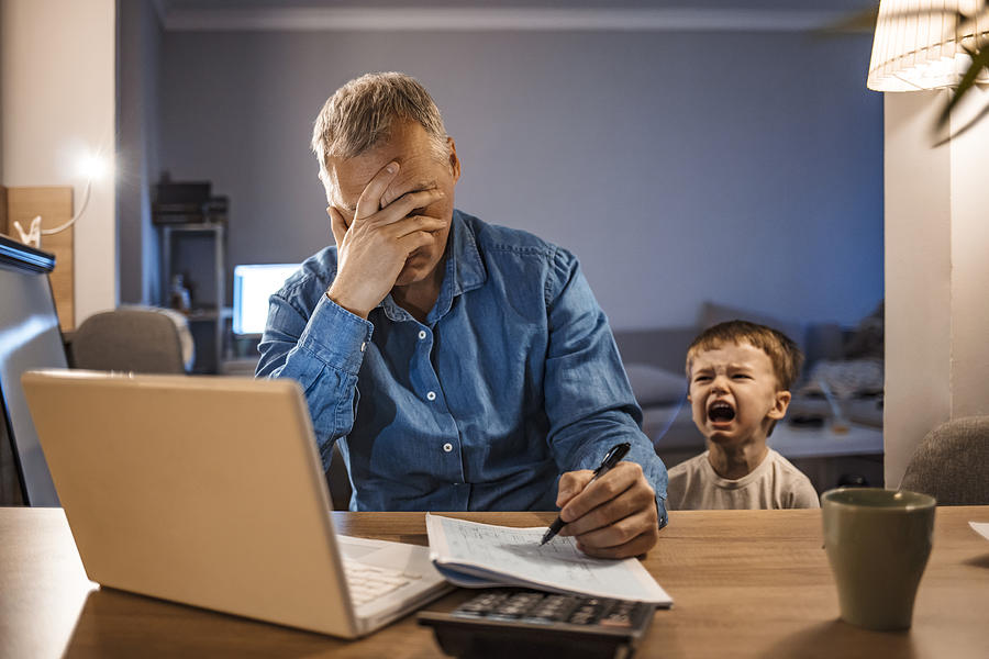 Stressed Man With his two years old son Working From Home Photograph by Ljubaphoto