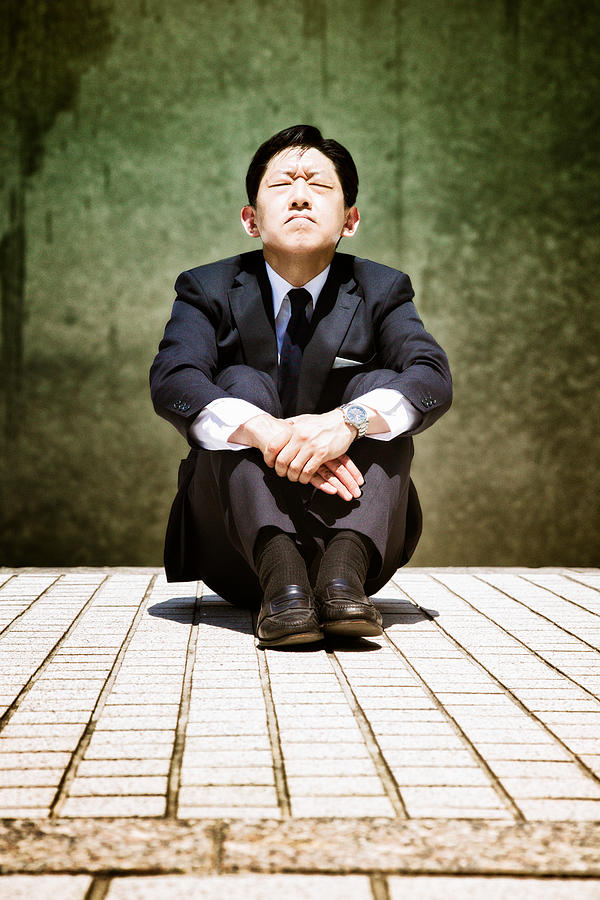 Stressed-out Japanese buisinessman sits and prays eyes closed Photograph by NicolasMcComber