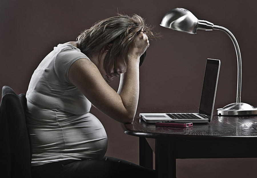 Stressed pregnant business woman sitting at desk in front of laptop Photograph by Justin Paget