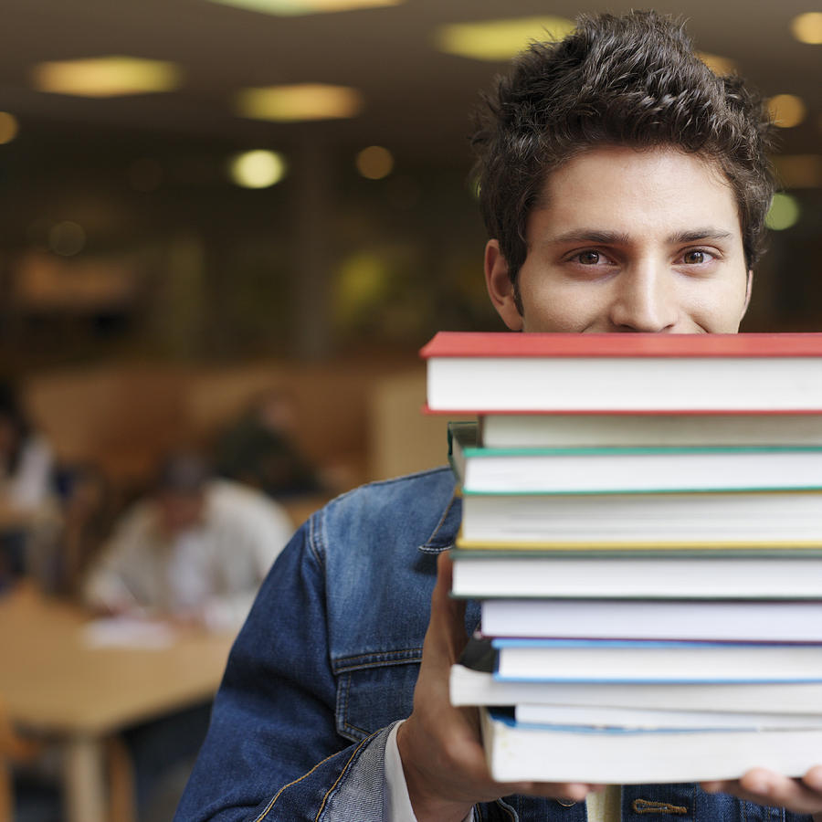 Student holding books in front of face in library, portrait Photograph by Stockbyte
