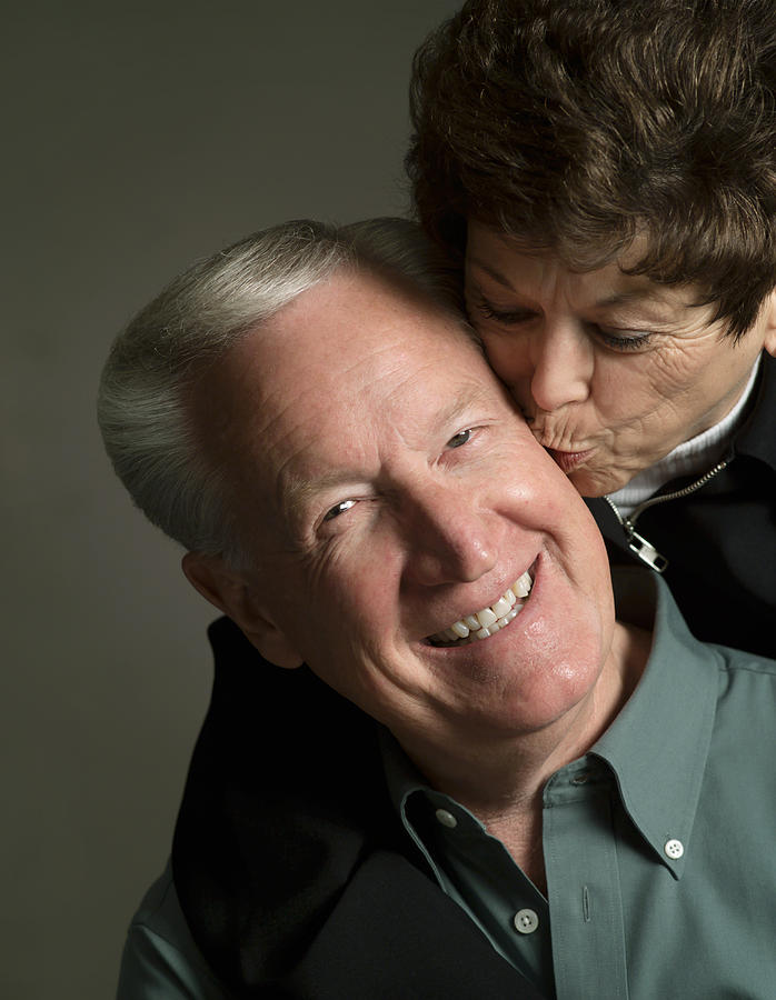 Studio Portrait Of An Elderly Caucasian Couple As The Woman Kisses The Cheek Of The Man Photograph by Photodisc
