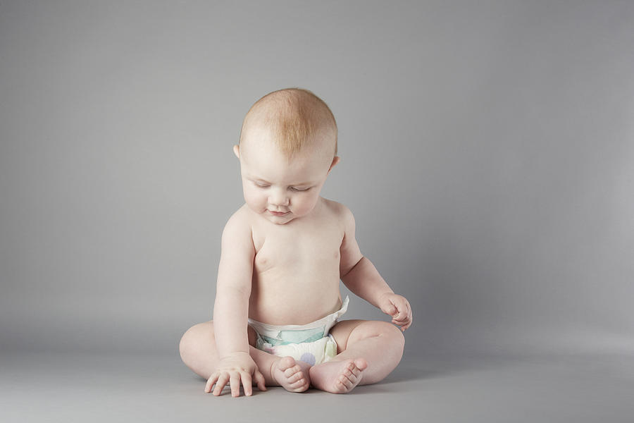 Studio portrait of baby boy sitting up and touching floor Photograph by Emma Kim