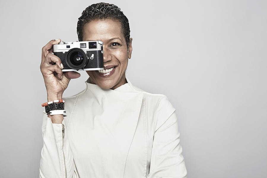 Studio portrait of happy mature woman holding up camera Photograph by Jpm