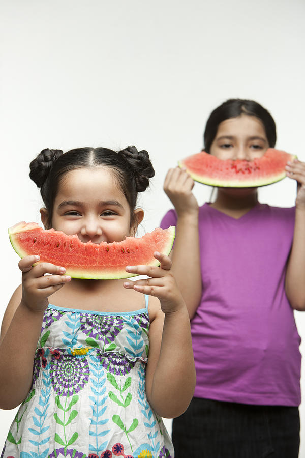 Studio portrait of two sisters (6-11) eating watermelon Photograph by ImagesBazaar