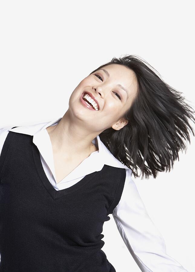 Studio shot of Asian woman tossing hair and smiling Photograph by Tanya Constantine