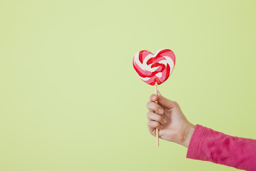 Studio shot of girls (10-11) hand holding heart-shaped lollipop Photograph by Vstock LLC
