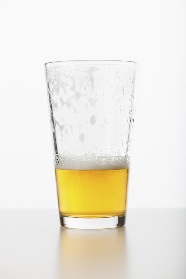 Studio shot of half full beer glass Photograph by Tetra Images