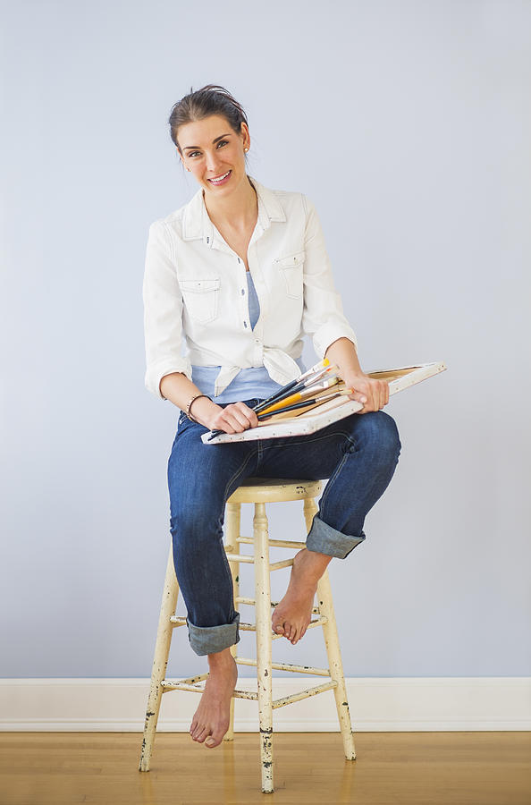 Studio Shot of woman sitting on stool, holding paintbrushes and artists canvas Photograph by Daniel Grill