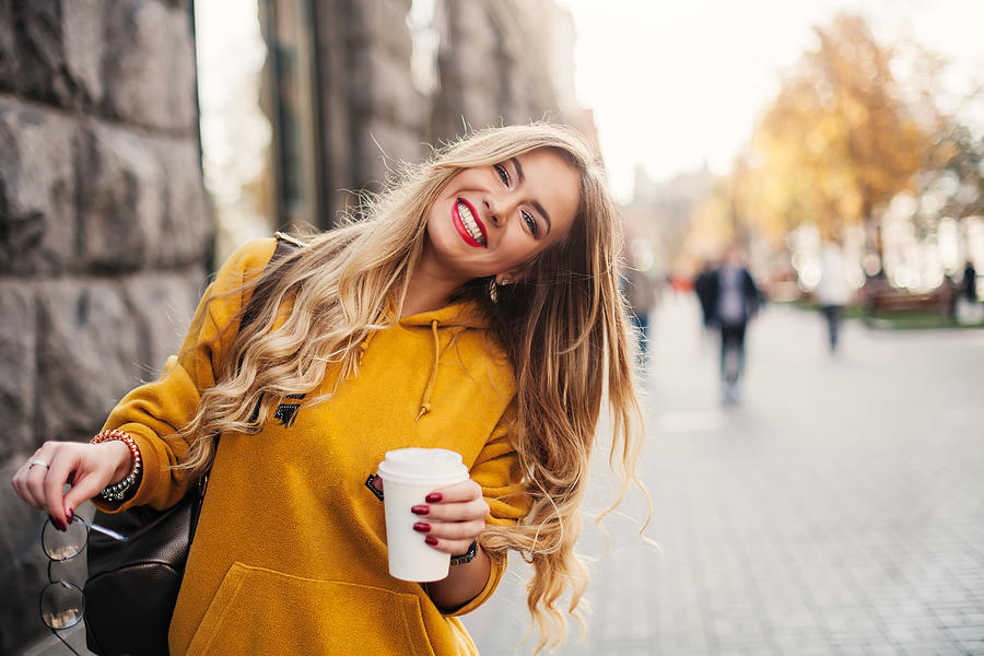 Stylish happy young woman wearing boyfrend jeans, white sneakers bright yellow sweetshot.She holds coffee to go. portrait of smiling girl in sunglasses and with bag Photograph by Natalia_Grabovskaya