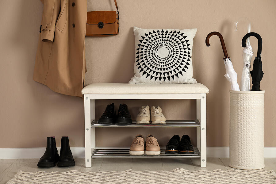 Stylish storage bench with different pairs of shoes near beige wall in hall Photograph by Liudmila Chernetska