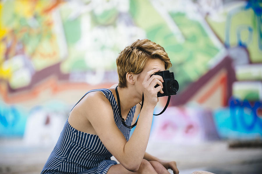 Stylish teenage girl photographing with camera in front of graffiti wall Photograph by Pete Saloutos