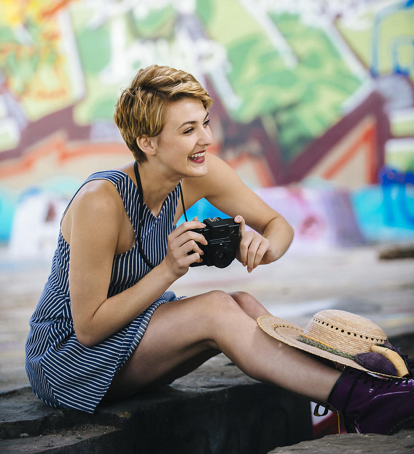 Stylish teenage girl sitting on sidewalk with camera in front of graffiti wall Photograph by Pete Saloutos