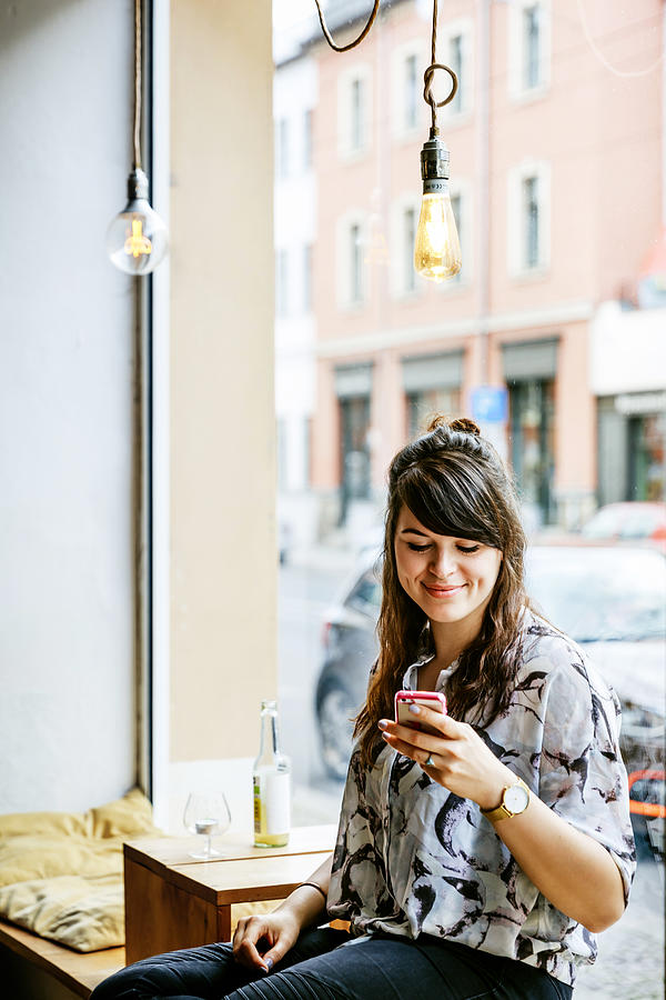 Stylish Young Woman Looking At Smartphone In Cafe Photograph by Tom Werner