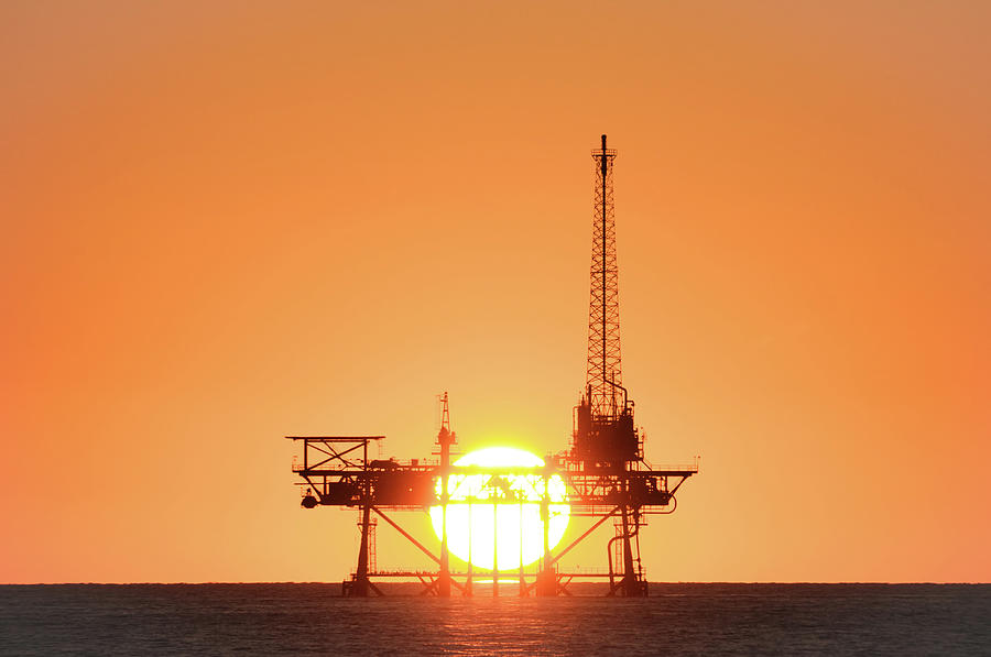 Sunset behind oil rig Photograph by Bradford Martin