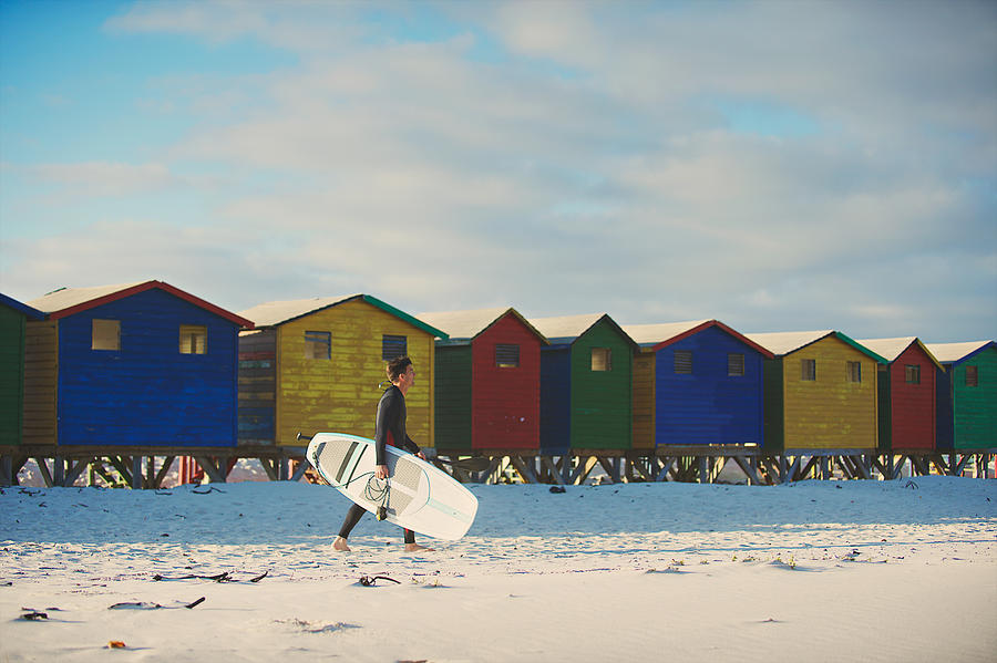 Surfer walking with surfboard with colourful beach huts Photograph by Wilpunt