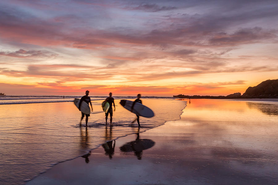 Surfers at sunset walking on beach, Costa Rica Photograph by Matteo Colombo