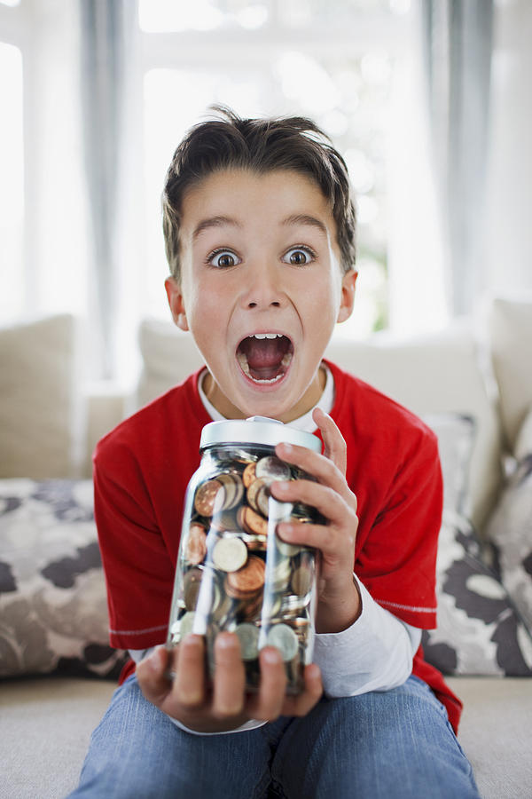 Surprised boy holding jar full of coins Photograph by Paul Bradbury