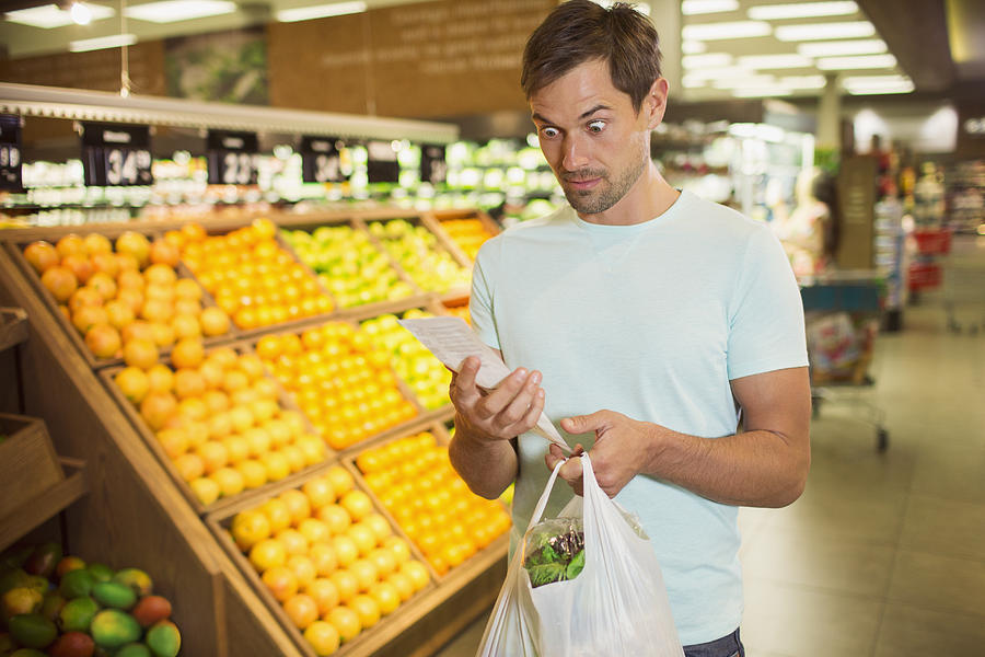Surprised man reading receipt in grocery store Photograph by Dan Dalton