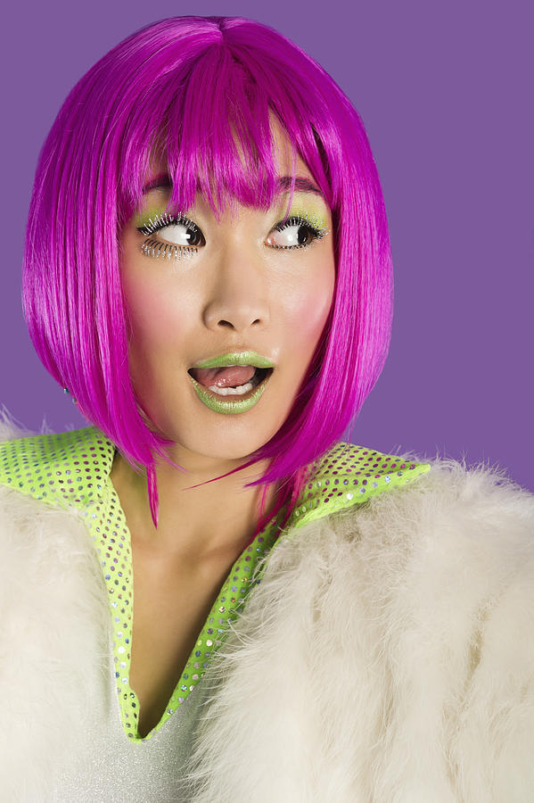 Surprised young funky woman in pink wig looking sideways over purple background Photograph by Moodboard