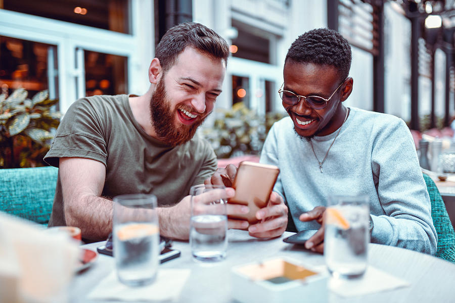 Swedish Male Laughing While Browsing Social Media With His African Friend Photograph by AleksandarGeorgiev