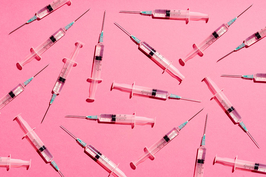 Syringe with injection or vaccine repetition pattern on pink background Photograph by Volanthevist