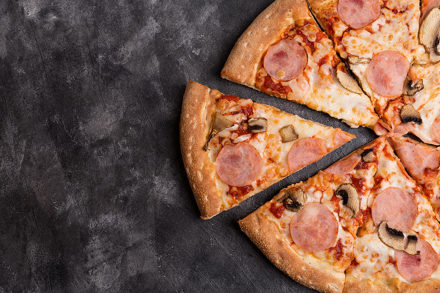 Tasty sliced pizza on black concrete background. Top view of hot pizza. With copy space for text, flat lay. Fast homemade food, home delivery. Photograph by Yulia Naumenko