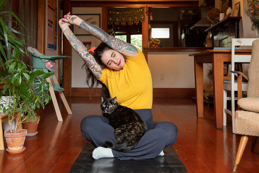 Tattooed woman stretching at home with cat in lap Photograph by Jessie Casson