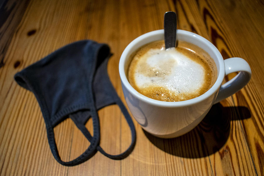 Taza de café con leche y tapaboca (barbijo) sobre mesa de madera Photograph by Javier Ghersi