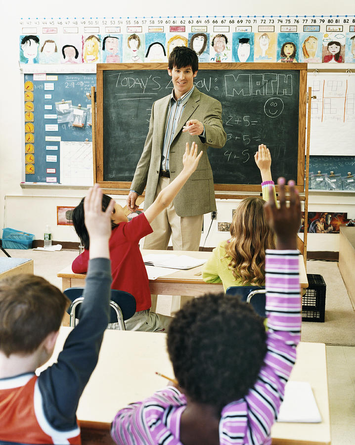 Teacher in a Classroom Pointing at Pupils With Raised Hands Photograph by Digital Vision.