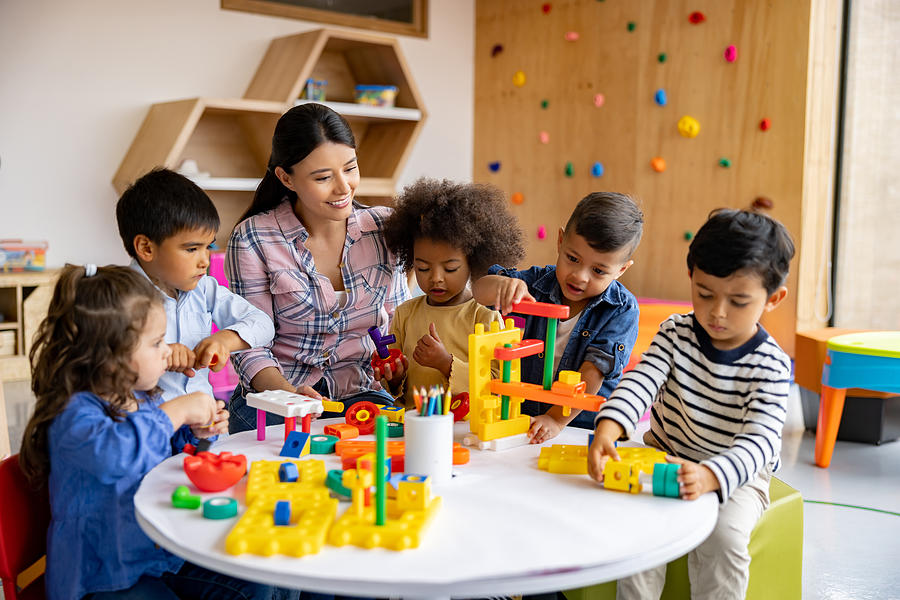 Teacher with a group of elementary students playing with toy blocks Photograph by Hispanolistic