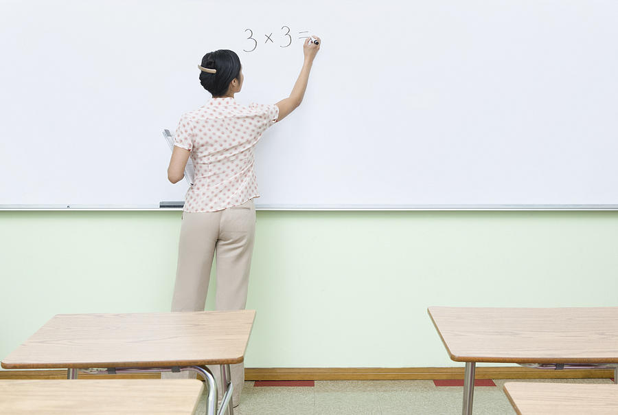 Teacher writing multiplication problem on whiteboard Photograph by Monashee Frantz