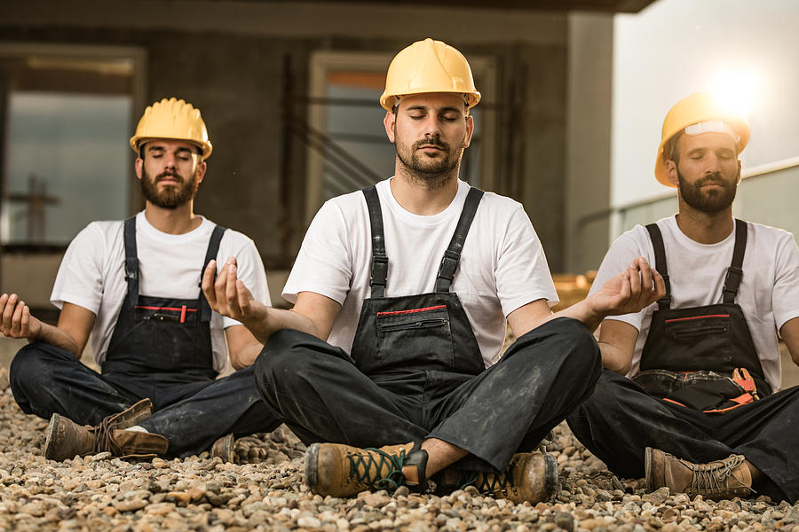 Team of manual workers meditating on a terrace of a construction site. Photograph by Skynesher