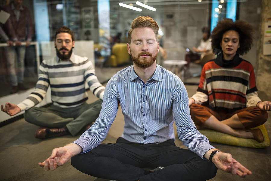 Team of relaxed business people exercising Yoga at casual office. Photograph by Skynesher