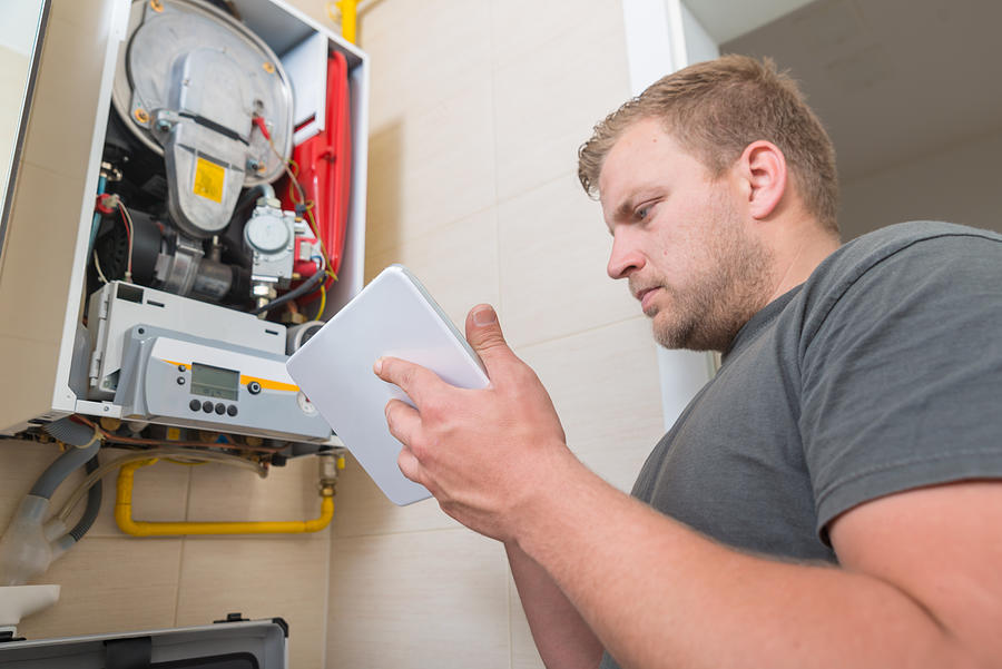 Technician repairing Gas Furnace using digital tablet Photograph by GregorBister