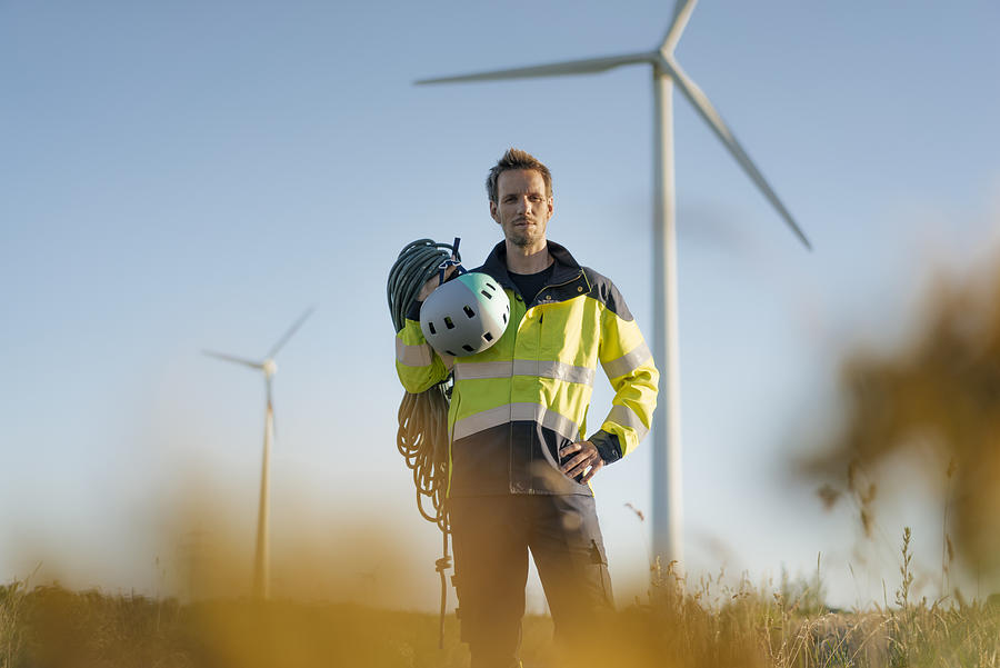 Technician standing in a field at a wind farm with climbing equipment Photograph by Westend61