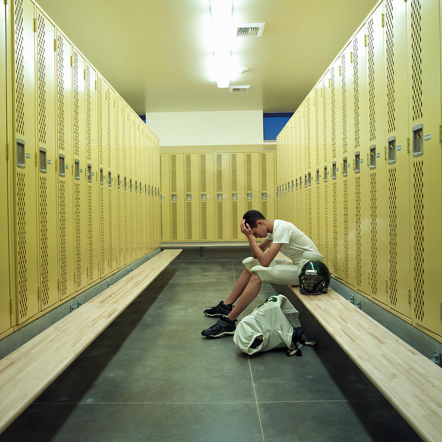 Teenage boy (15-17) in football uniform, sitting in locker room Photograph by F64