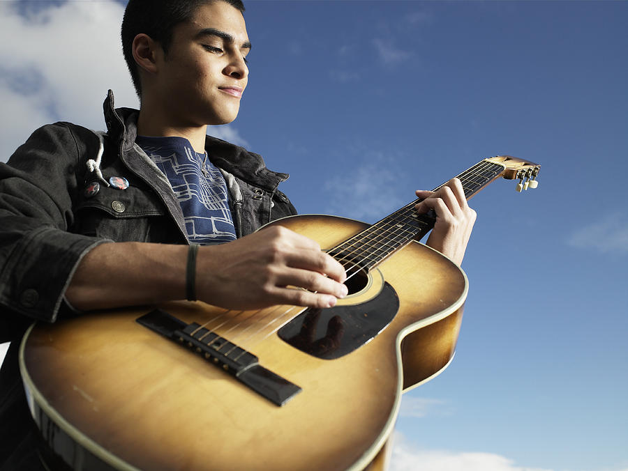 Teenage boy (15-17) playing guitar, low angle view Photograph by Ryan McVay