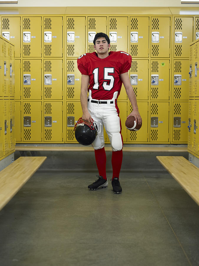 Teenage boy (16-18) dressed for football,  standing in locker room Photograph by Thomas Barwick