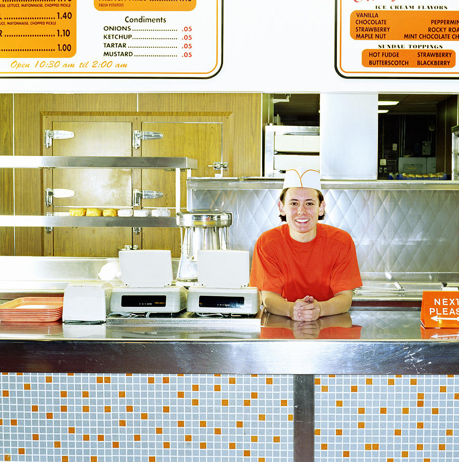 Teenage boy (17-19) working behind counter of fast-food restaurant Photograph by Andersen Ross