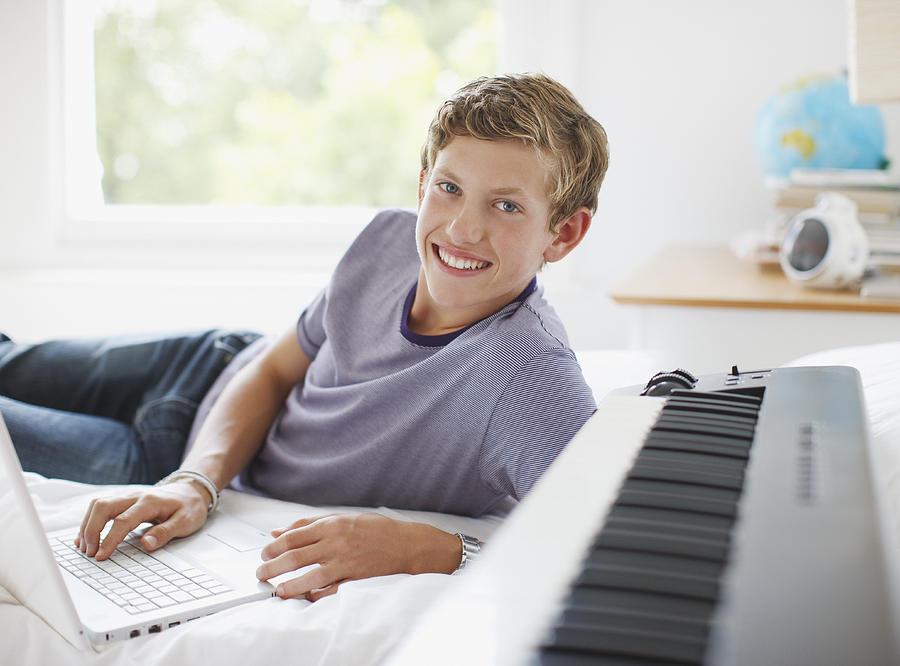 Teenage boy laying on bed with laptop and electronic piano keyboard Photograph by Paul Bradbury