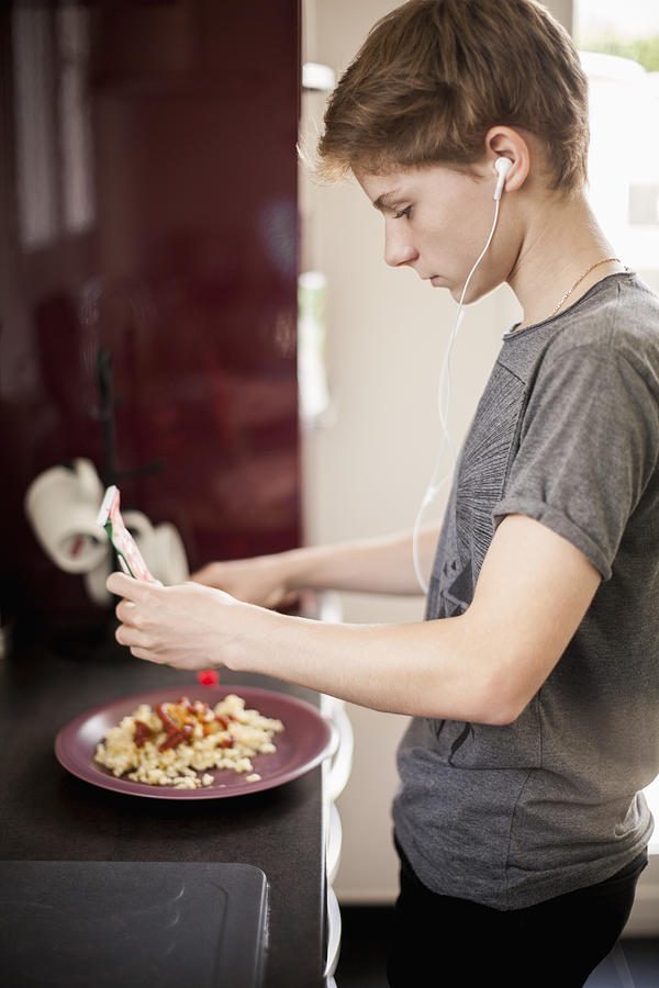 Teenage boy listening to music with breakfast Photograph by Letizia Le Fur