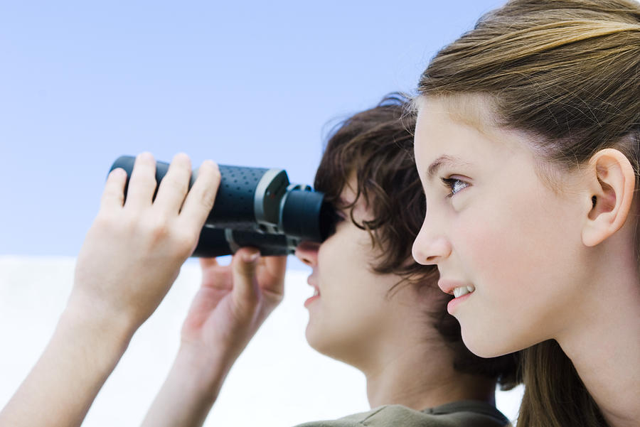 Teenage boy looking away through binoculars, sister nearby, profile Photograph by PhotoAlto/Michele Constantini